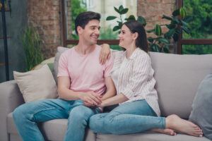 Couple sitting together on a couch, looking thoughtful and supportive