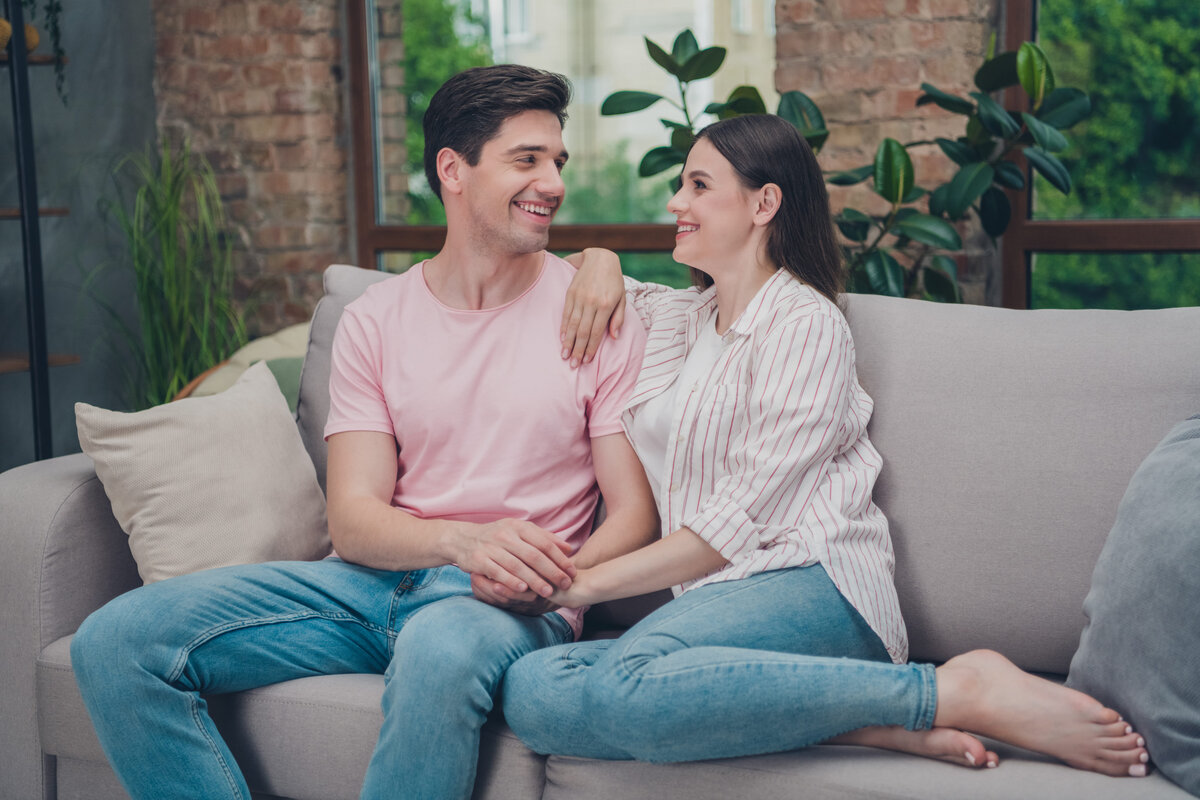 Couple sitting together on a couch, looking thoughtful and supportive
